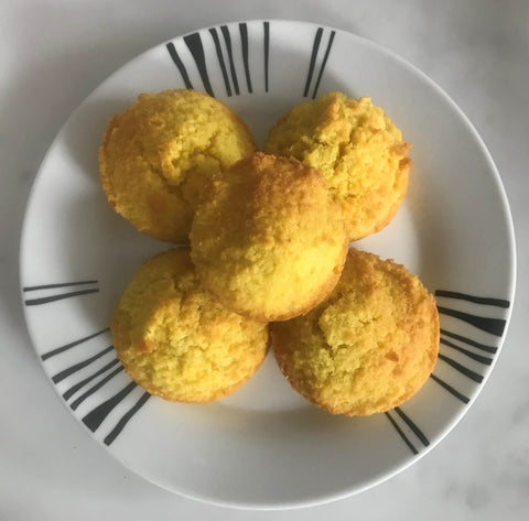 Golden Turmeric and ginger muffins stacked on a round white plate with black striped detailing. Plate is on a marble countertop. 